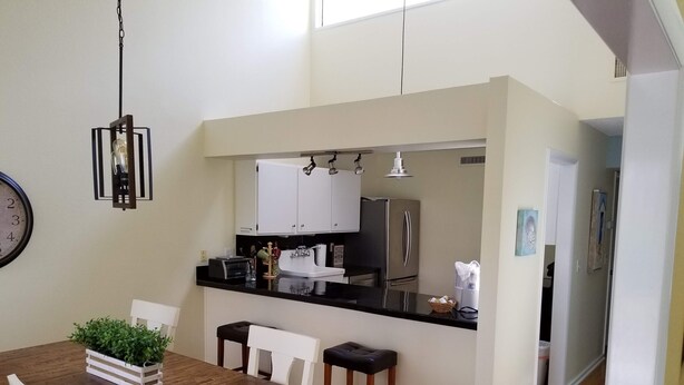 A modern kitchen with white cabinets, a stainless steel refrigerator, and a black countertop. There is a dining table with chairs and a small island with stools. - SAWGRASS PONTE VEDRA BEACH (Ponte Vedra Beach)