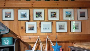 Een muur met ingekaderde foto's, een magnetron en een houten plank met flessen.