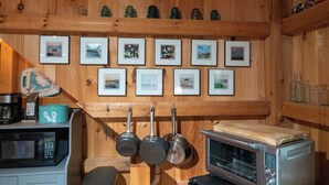 Een keuken met houten wanden, een magnetron, een heteluchtoven, hangende pannen en ingelijste foto's aan de muur.