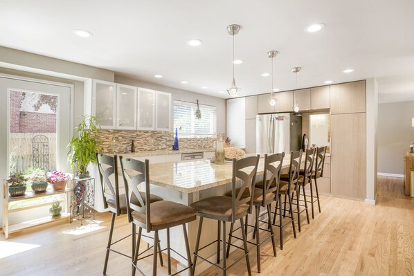 A modern kitchen with a large island, bar stools, and pendant lighting.