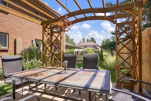 An outdoor patio with a pergola structure, a table, and two chairs.