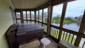 A hot tub on a wooden deck with a view of a body of water and houses in the background.
