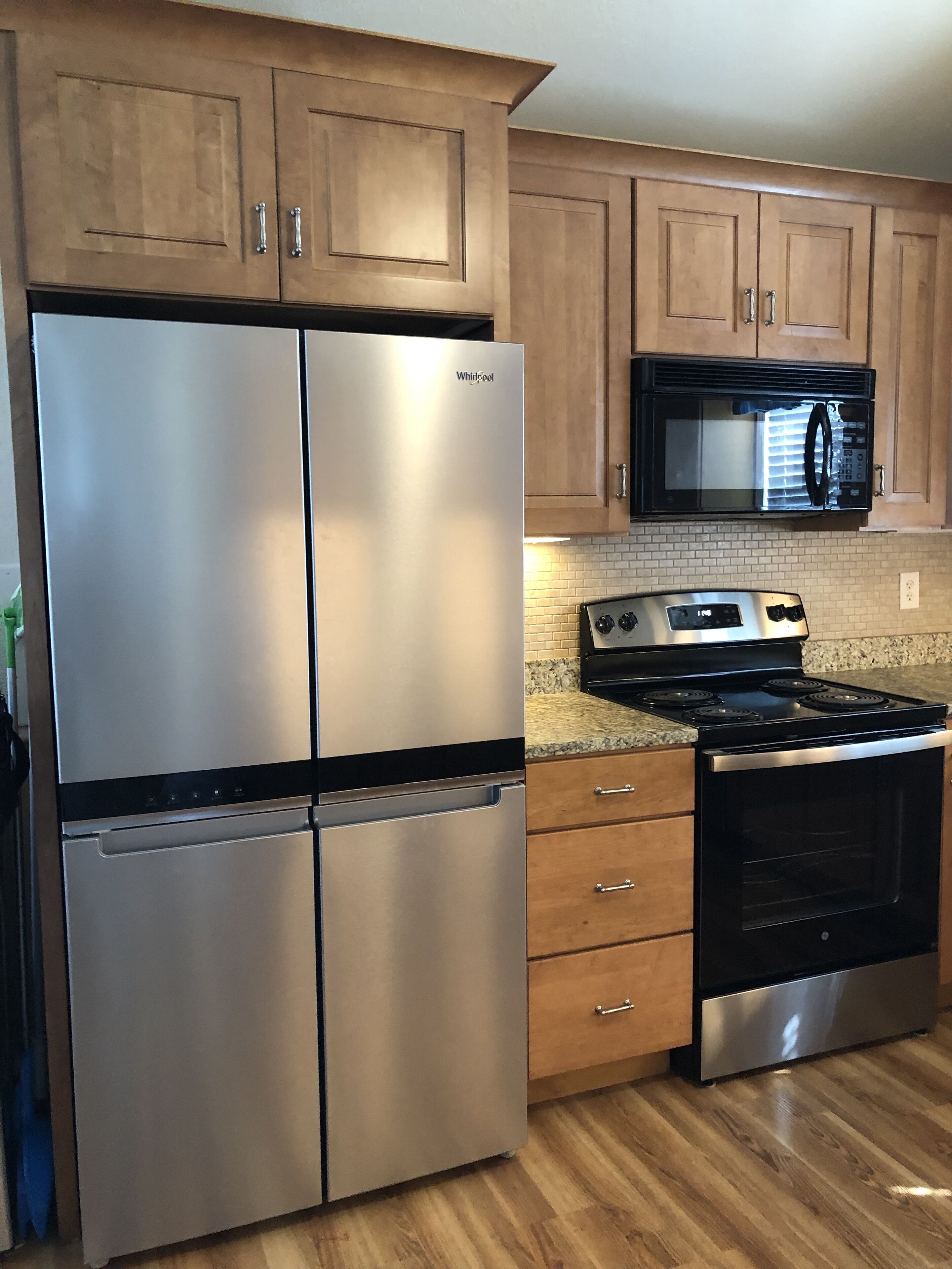 A kitchen with stainless steel appliances, wooden cabinets, a granite countertop, and a black microwave.