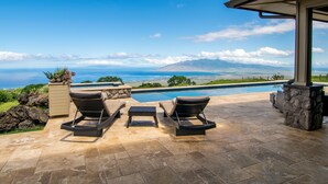A poolside area with lounge chairs and a stone planter, overlooking a scenic view of the ocean and distant mountains. - Kula Luxury Retreat With Stunning Ocean & Mountain Views! (Kula)