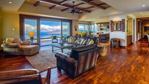 A spacious living room with a large window offering a view of the ocean, a fireplace, and a dining area with a kitchen in the background. - Kula Luxury Retreat With Stunning Ocean & Mountain Views! (Kula)