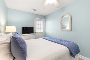 A bedroom with a bed, a television, a dresser, a mirror, and a window with blinds.