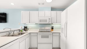 Una cocina con armarios blancos, microondas, horno, fregadero y cafetera.