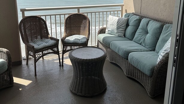 A balcony with wicker furniture, a round table, and a sofa with cushions.
