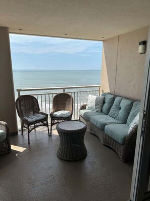 A balcony with wicker furniture, a round table, and a sofa with cushions. -   DESIGNER BEACH PENTHOUSE, 1900 SQ FT, N&S VIEWS, WIFI, 2 BALCONIES,  ALL EXTRA (North Myrtle Beach)