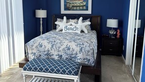 A bedroom with a bed, a bench, a nightstand, a lamp, and a painting on the wall.