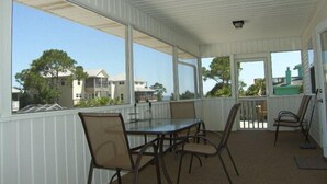 A covered patio with a table and chairs, large windows, and a view of houses and trees. - Southern Tide in Indian Pass 😊 (Indian Pass)