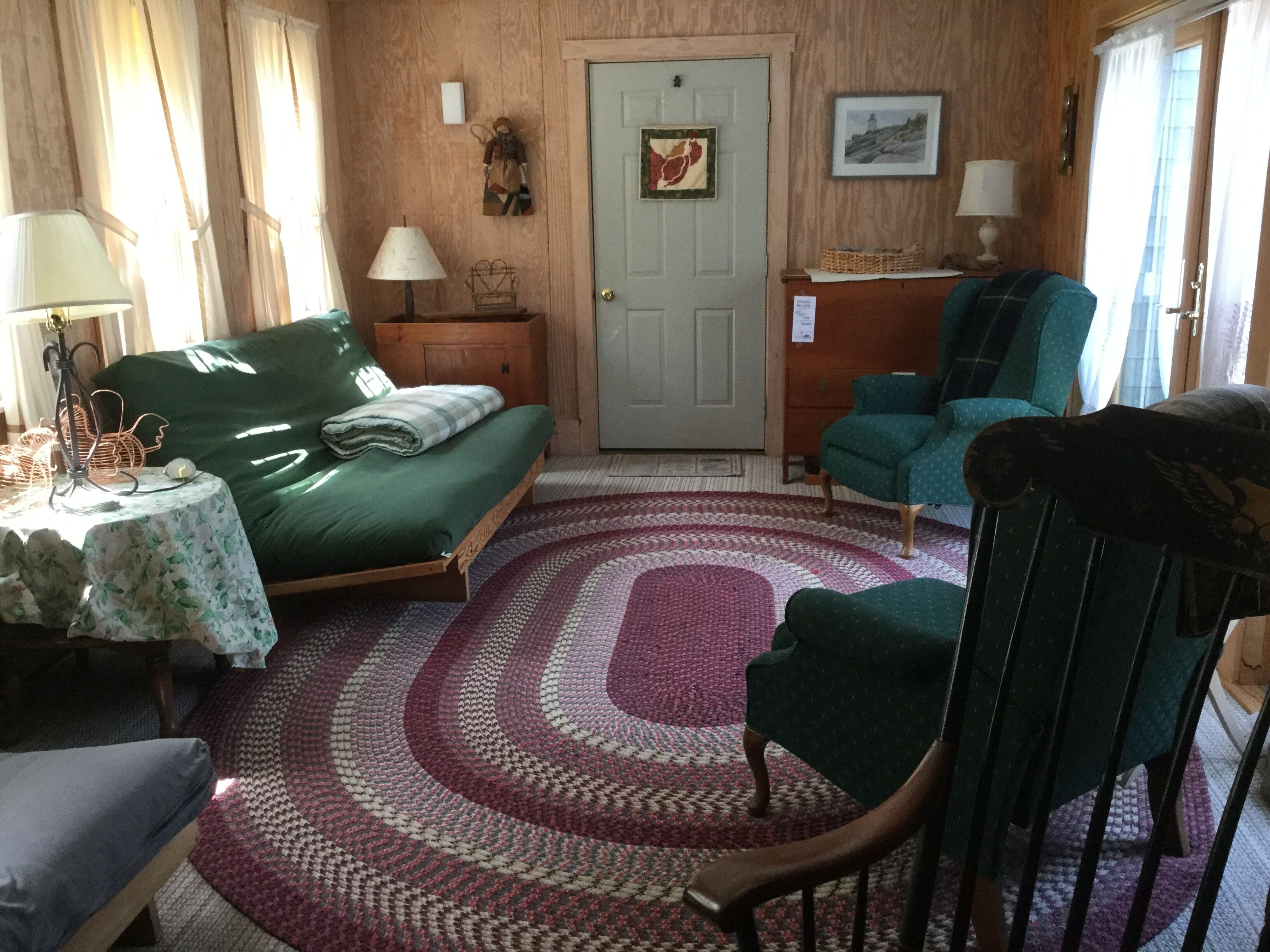 A cozy room with a bed, a chair, a table with a lamp, and a door.