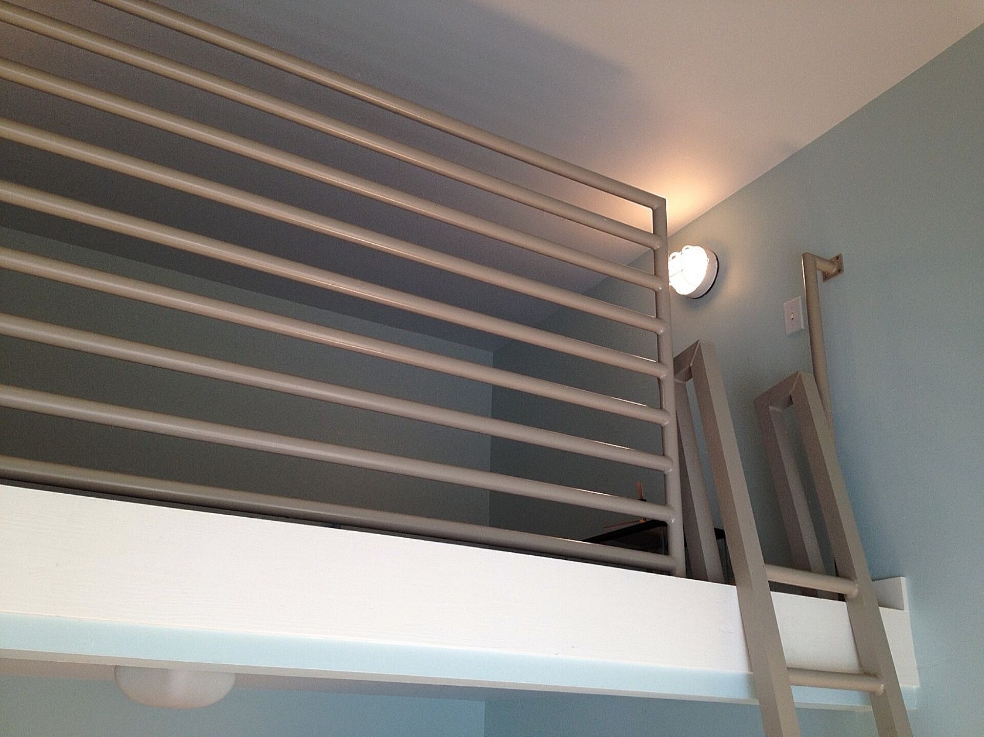 A bunk bed with a ladder, a wall-mounted light, and a window.
