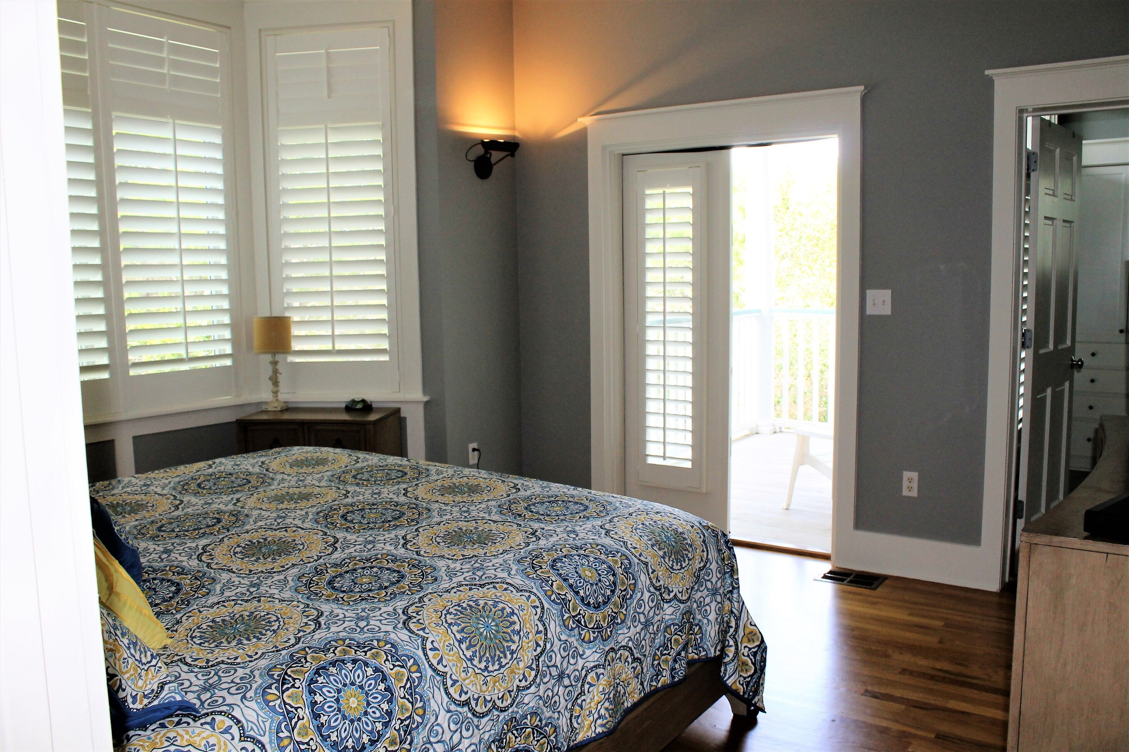 A bedroom with a large bed, a nightstand, a lamp, and a door leading to a balcony.