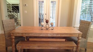 A wooden dining table with a bench, surrounded by wicker chairs, in a room with a staircase and a window with blinds. - 5 BR, 5 BA in Seaside, quick walk to the private beach access or main pool  (Santa Rosa Beach)