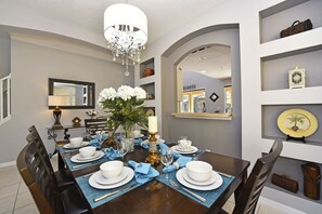 A dining room with a dark wooden table set for four, blue placemats, white plates, and a chandelier.