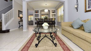 A spacious living room with a round glass coffee table, a beige sofa, and a dining area with a chandelier. - TOP REVIEWED HOME! Only 3 MILES to Disney, South Pool in Emerald Island Resort (Kissimmee)