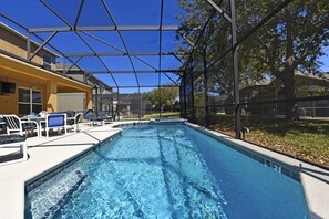 A swimming pool with a covered area, lounge chairs, and a view of the surrounding neighborhood.