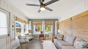 Uma sala de estar bem iluminada com ventilador de teto, sofá, mesa de centro e um espaço de jantar com cadeiras e uma pequena mesa.