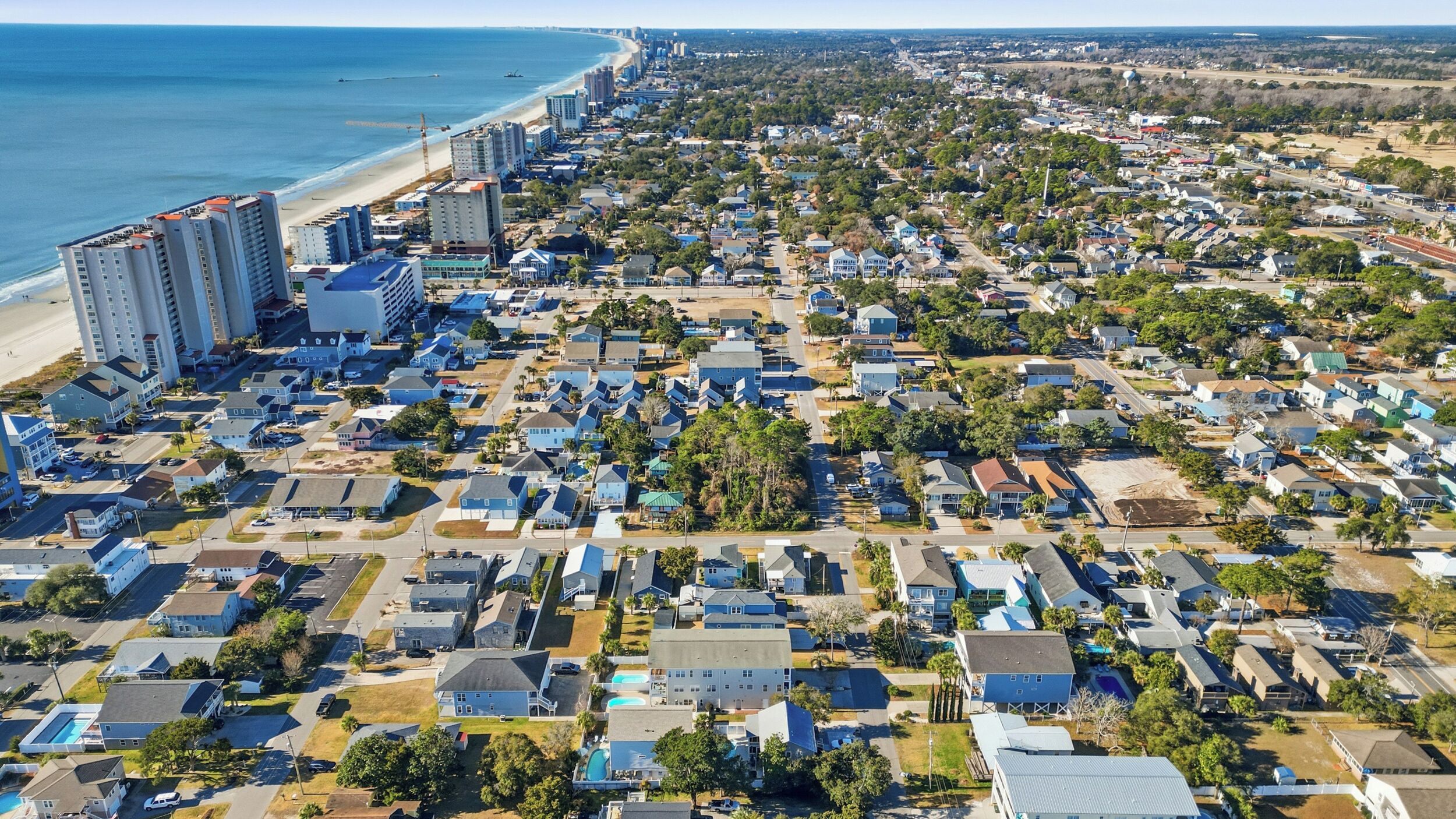 Vue aérienne d’un quartier résidentiel situé sur la côte, avec une plage, des habitations densément regroupées et des immeubles de grande hauteur.