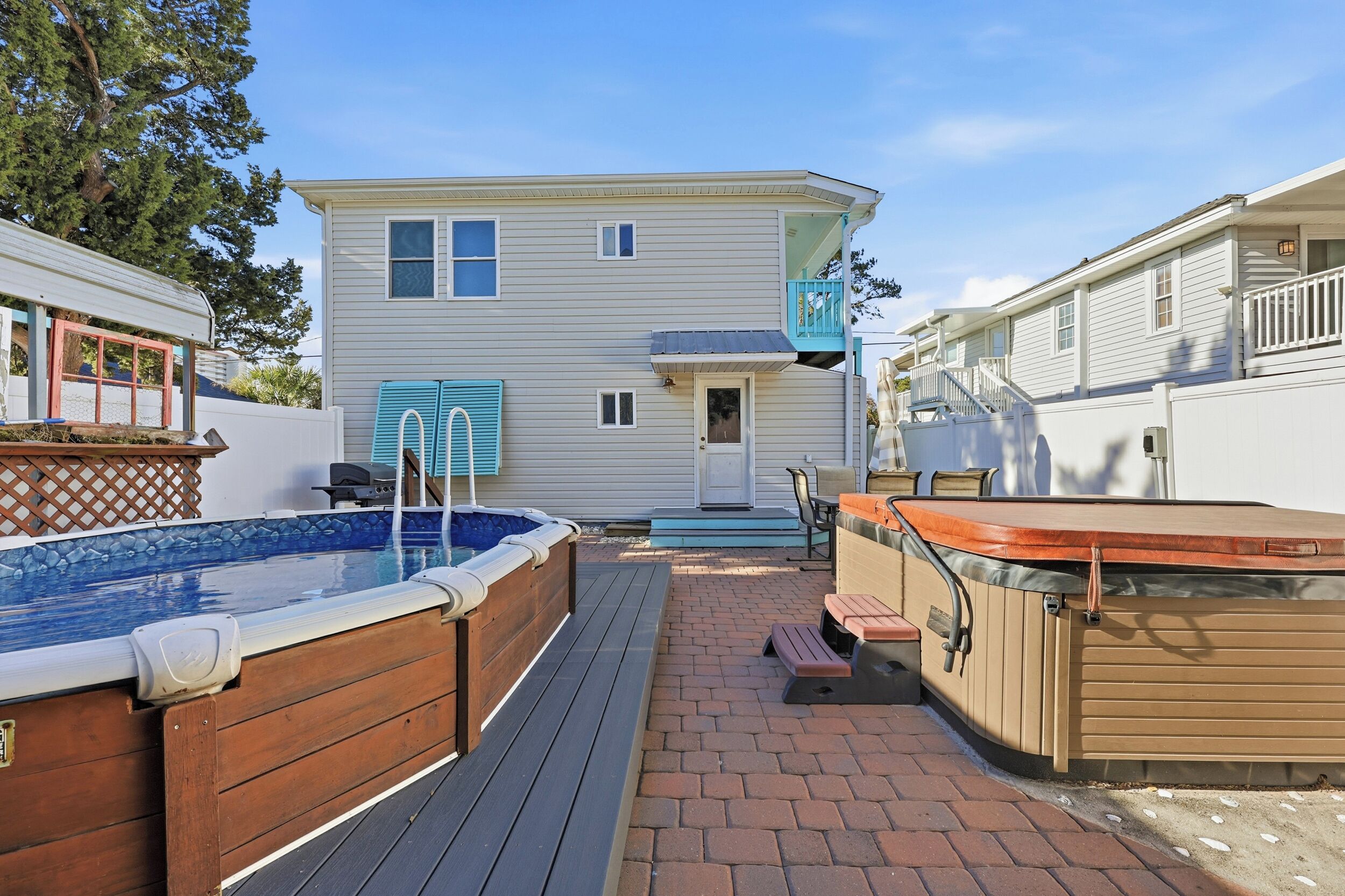 A backyard with a hot tub, a wooden deck, and a house with a balcony.