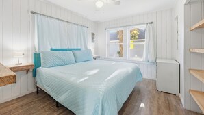 Quarto com cama, ventilador de teto, janela com cortinas e radiador.