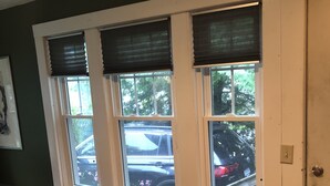 A room with a wooden floor, a window with blinds, a small wooden stool, and a door.