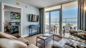 Ein Zimmer mit Bett, Fernseher, Sofa, Couchtisch und einem Balkon mit Blick auf den Strand.