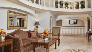 Eine geräumige Lobby mit hoher Decke, einem großen Spiegel, einem Sofa, einem Couchtisch und einem an der Wand befestigten Fernseher.