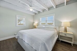 A bedroom with a bed, two bedside tables with lamps, a ceiling fan, and two windows with blinds.