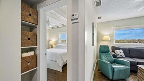 A bedroom with a bed, a teal chair, a grey sofa, and wicker baskets on shelves.