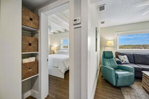 A bedroom with a bed, a teal chair, a grey sofa, and wicker baskets on shelves.