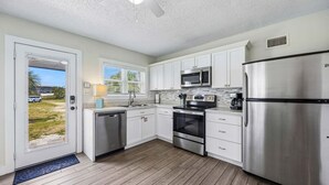 A modern kitchen with white cabinets, stainless steel appliances, and a wooden floor.