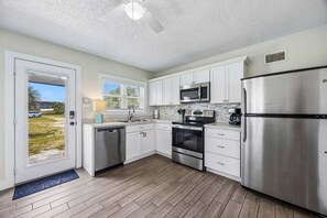 A modern kitchen with white cabinets, stainless steel appliances, and a wooden floor.