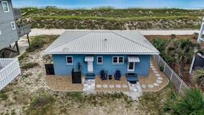 A beachfront house with a blue exterior, a covered patio with two chairs, and a view of the ocean.