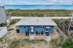 A beachfront house with a blue exterior, a covered patio with two chairs, and a view of the ocean.