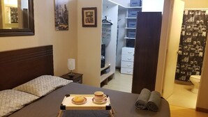 Une chambre d’hôtel avec un lit, une table de chevet sur laquelle se trouve un plateau de petit-déjeuner, une armoire et une salle de bain visible à travers une porte ouverte.