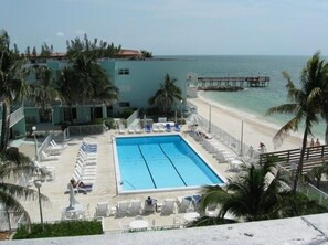 Un espace piscine avec des chaises longues, une piscine et une vue sur la plage.