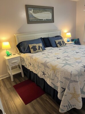 A bedroom with a bed, nightstands, a red rug, and a wall-mounted picture. - Gulf Front-private beach -west end unit-  sunsets from unit! August reduced!! (Seacrest)