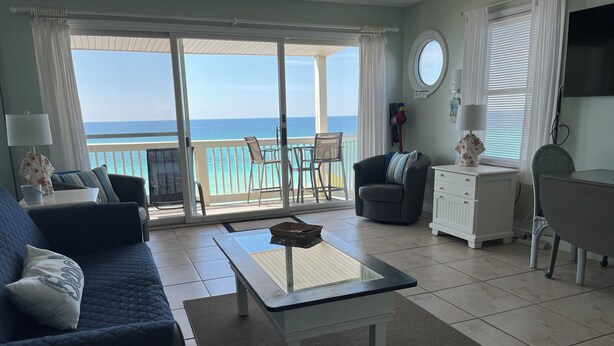 A living room with a view of the ocean, a sofa, a coffee table, a TV, and a small table with a lamp.