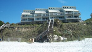 A beachfront hotel with multiple balconies and a staircase leading to the entrance.