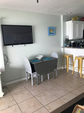 A dining area with a table, chairs, a television, and kitchen cabinets. - Gulf Front-private beach -west end unit-  sunsets from unit! August reduced!! (Seacrest)