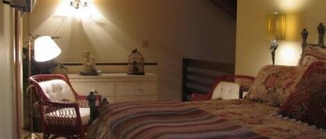 Een knus slaapkamer met een groot bed, een kast, een stoel en een lamp.
