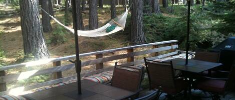 Una terraza al aire libre con una hamaca, sillas y mesas de madera bajo sombrillas.