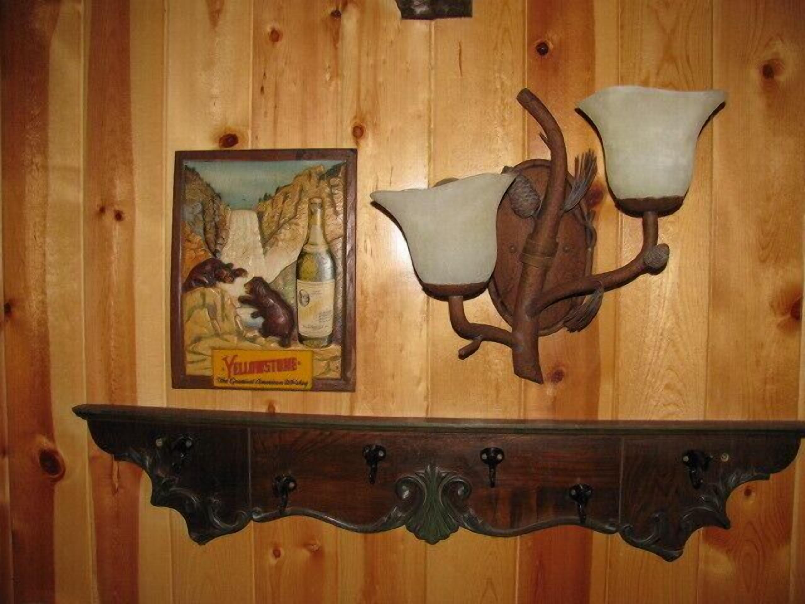 Pareti in legno con una cornice che ritrae un orso e una bottiglia, un lampadario a parete e uno scaffale in legno con ganci.