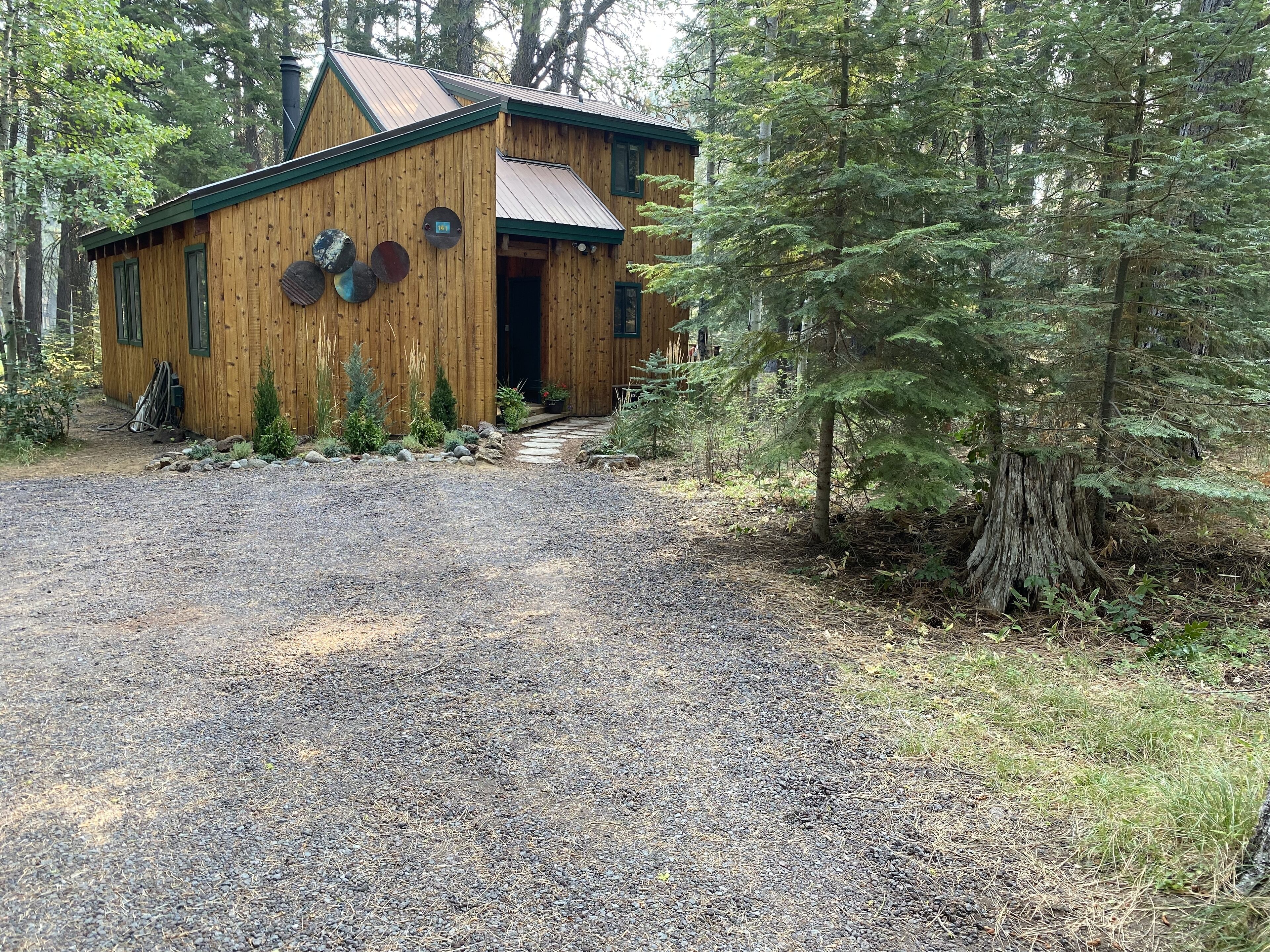 A wooden cabin with a gravel driveway, surrounded by trees.