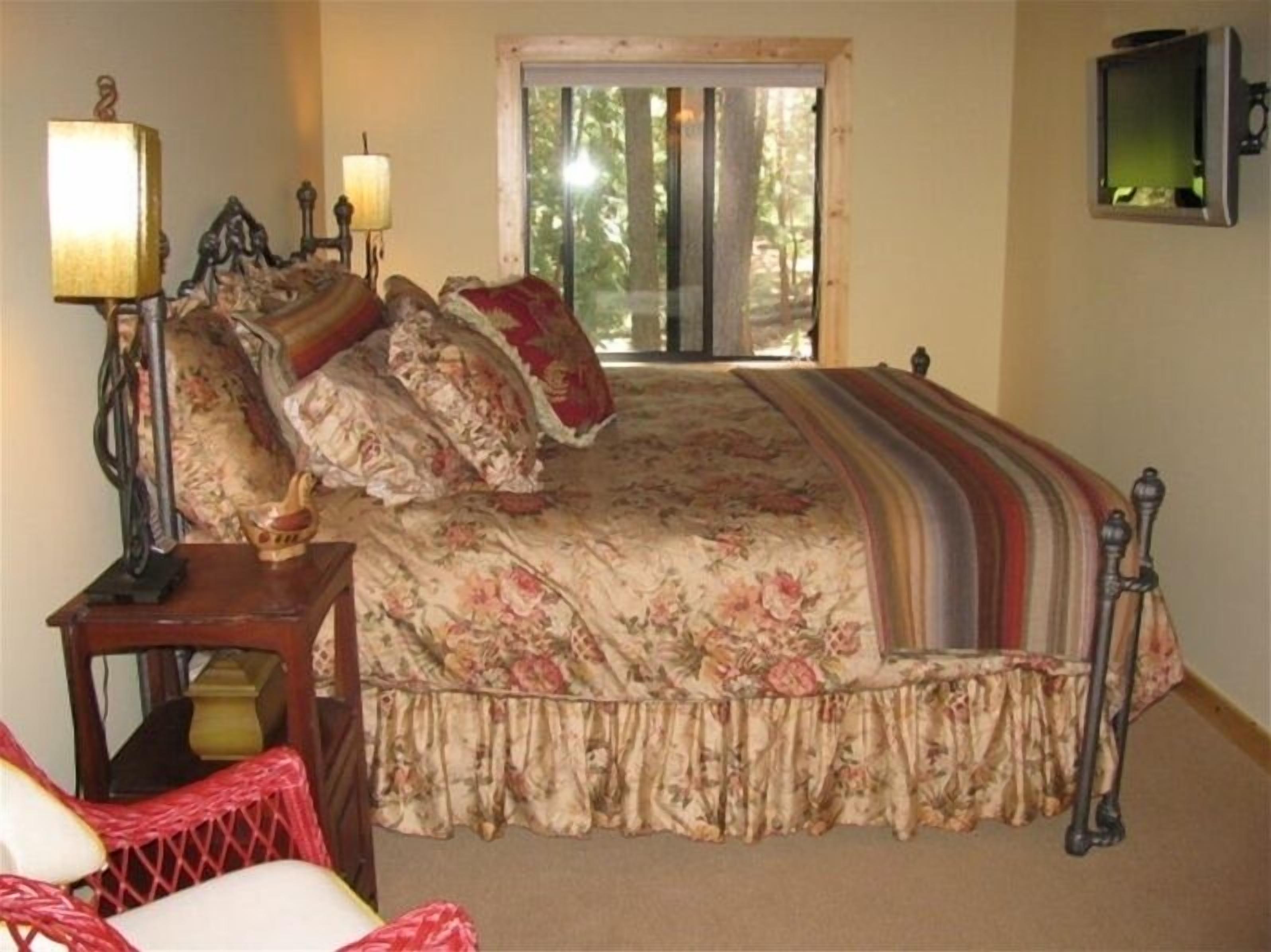 Ein Schlafzimmer mit einem großen Bett, zwei Nachttischlampen, einem Sessel und einem Fenster mit Blick auf Bäume.