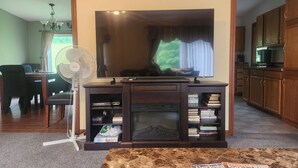 A living room with a flat-screen TV, a fireplace, a dining area with a table and chairs, and a kitchen area with wooden cabinets. - 2400sf Secluded Family Mountain House 16 Acres- 2 min to Jiminy Peak- near Lenox (Hancock)