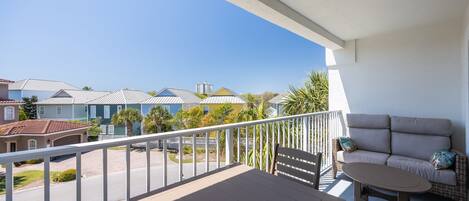 A balcony with a sofa and table, overlooking a residential area with houses and a clear sky.