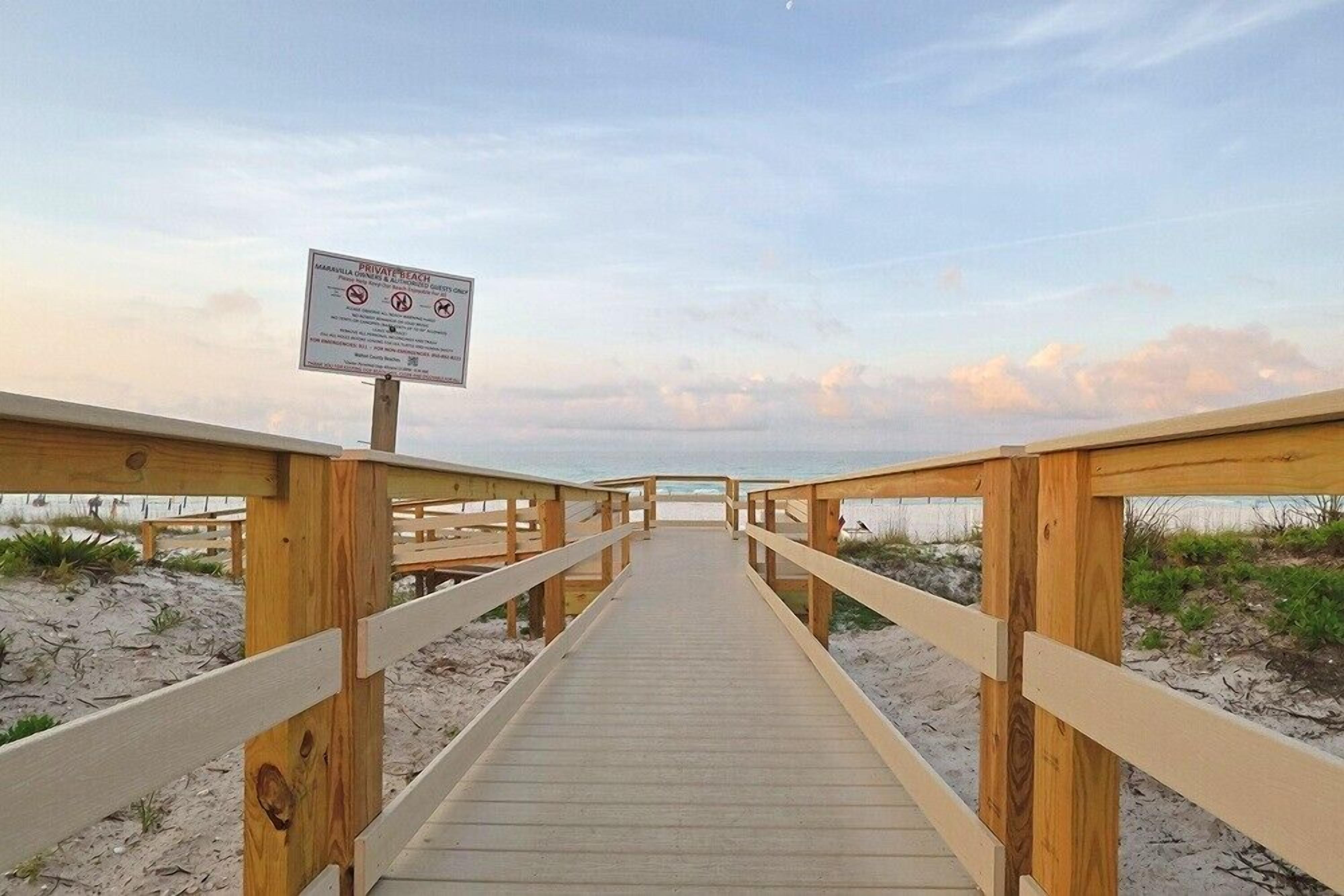Une promenade en bois mène à une plage où un panneau indique qu’il s’agit d’une plage privée.